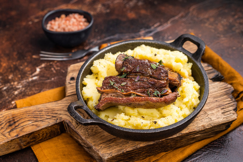 Caramelized beef short ribs resting on creamy mashed potatoes, served on a rustic plate with a warm brown background, top view